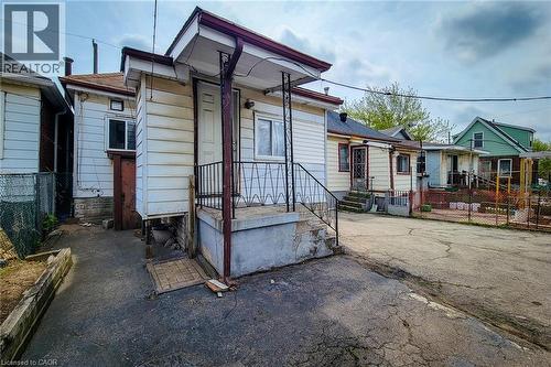 Rear exterior featuring a covered porch with metal railing, white siding, and a paved surface - 463 Wellington Street N, Hamilton, ON - Outdoor