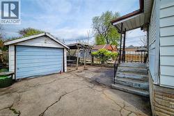 Detached garage with light blue garage door, concrete driveway, stone veneer foundation, covered porch with black metal railing, and a wooden pergola structure - 