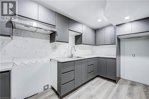 Modern kitchen featuring gray flat-panel cabinetry, light-toned countertops, a stainless steel undermount sink with a gooseneck faucet, and white patterned backsplash tiling - 2367 Middlesmoor Crescent, Burlington, ON - Indoor Photo Showing Kitchen