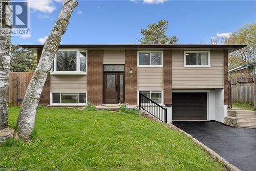 A bungalow featuring a brick and siding exterior, bay window, front entry with sidelight, integrated garage, and a sloped front lawn with mature trees - 176 Woodville Place, Waterloo, ON - Outdoor