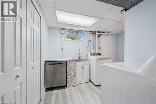 Dedicated laundry area featuring wood-finish flooring, a utility sink with a chrome faucet, white cabinetry, and a window providing natural light - 176 Woodville Place, Waterloo, ON - Indoor Photo Showing Laundry Room