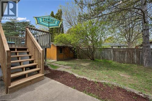 Expansive outdoor living area featuring a wood deck with stairs, a spacious lawn, a wooden privacy fence, a storage shed, and mature trees - 176 Woodville Place, Waterloo, ON - Outdoor