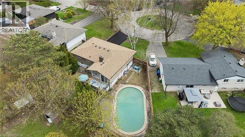 Oval-shaped in-ground pool with surrounding paved patio, situated beside a multi-level residential structure featuring a light brown shingle roof and a brick chimney - 176 Woodville Place, Waterloo, ON - Outdoor With View