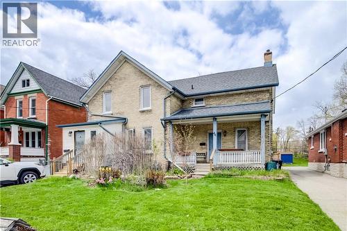 Brick exterior home featuring a covered front porch with white railing, a side entrance with wooden steps, a green lawn, and a paved driveway - 46 Shanley Street, Kitchener, ON - Outdoor With Deck Patio Veranda
