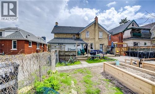 Rear exterior featuring a two-story brick construction, a ground-level wood deck, a patio area with pavers, a grass lawn, and raised garden beds - 46 Shanley Street, Kitchener, ON - Outdoor
