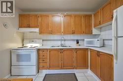 Kitchen featuring wood-finish cabinetry, white appliances, white tiled flooring, white tiled backsplash, and a double basin sink - 