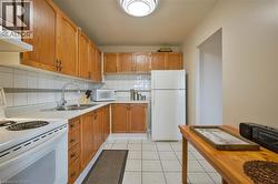 Kitchen featuring wood-finish cabinetry, white tile flooring, white tile backsplash with a grey accent band, a double basin stainless steel sink, and a white refrigerator - 