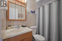 Bathroom featuring a wood-finish vanity with an integrated sink, a chrome two-handle faucet, a triple-mirror medicine cabinet with a wood-finish frame, and overhead vanity lighting - 
