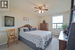 Carpeted room featuring a ceiling fan with integrated lighting, a large window, a decorative wooden headboard, a wooden dresser, and neutral-toned walls - 