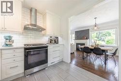Kitchen featuring white cabinetry, subway tile backsplash, stainless steel range with matching vent hood, and light-toned tile flooring - 