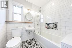 Bathroom featuring white subway tile walls, patterned floor tiles, a window with a wood shelf, a wall-mounted sink, and a bathtub with an integrated tiled niche - 