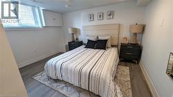 Bedroom featuring wood-finish flooring, a window with blinds, and built-in white cabinetry - 