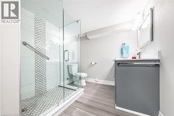 Contemporary bathroom featuring a glass-enclosed shower with decorative tile accent, a vanity with a white countertop, and wood-finish flooring - 