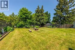 Expansive grassy yard featuring a fire pit, surrounding garden beds, and perimeter fencing - 