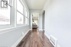 Hallway featuring a series of large windows with white trim, wood-finish flooring, light-toned wall paint, white baseboards, and a rounded archway - 