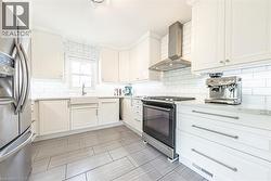 Kitchen featuring white shaker cabinetry, white subway tile backsplash, light-toned countertop, stainless steel appliances, and wood-finish tile flooring - 