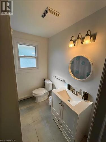 Bathroom featuring a white vanity with integrated sink, brushed nickel faucet, wall-mounted light fixture, rectangular window, and a toilet **Virtually Staged** - 148 Bishop Street S, Cambridge, ON 