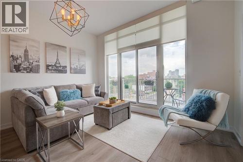 Living space featuring wood-finish flooring, a contemporary geometric chandelier, and full-height windows with roller shades - 191 King Street S Unit# 607, Waterloo, ON 