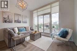 Living space featuring wood-finish flooring, a contemporary geometric chandelier, and full-height windows with roller shades - 