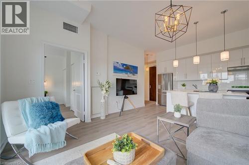 Open-concept living space featuring wood-finish flooring, a contemporary geometric chandelier, recessed lighting, and a white kitchen with pendant lights - 191 King Street S Unit# 607, Waterloo, ON 