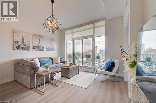Bright living area featuring wood-finish flooring, a contemporary geometric chandelier, and full-height glass doors leading to a balcony - 191 King Street S Unit# 607, Waterloo, ON 
