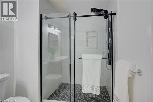 Spacious shower enclosure with black-framed glass sliding doors, black hexagonal tile flooring, and a built-in shower niche - 191 King Street S Unit# 607, Waterloo, ON 