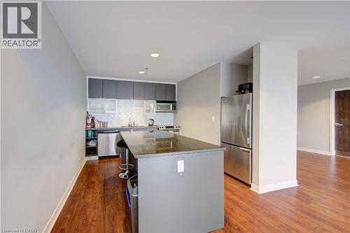 Building  Party Room Kitchen featuring an expansive island with a stone countertop, full-height subway tile backsplash, stainless steel appliances, and wood-finish flooring - 191 King Street S Unit# 607, Waterloo, ON 