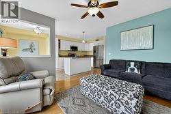 Open-concept living area featuring wood-finish flooring, a ceiling fan with integrated lighting, and a pass-through window to the adjacent kitchen - 