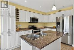 Kitchen featuring white shaker-style cabinetry, a built-in wine rack, stone-finish countertops, stainless steel appliances, and an island with a double basin sink - 