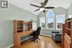 Vaulted ceiling with a ceiling fan light fixture, wood-finish flooring, and three large windows providing ample illumination - 