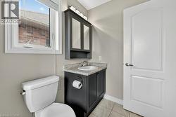 Bathroom featuring a white toilet, casement window, dark wood-finish vanity with an integrated sink, textured countertop, and wall-mounted medicine cabinet with integrated lighting - 