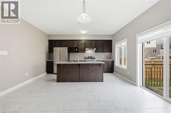 Open concept kitchen and dining area featuring light-toned flooring, dark wood cabinetry, a center island with a sink, and stainless steel appliances - 