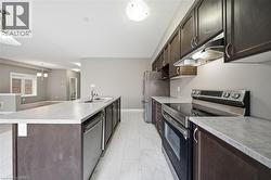 The kitchen features dark wood cabinetry, light-colored countertops, stainless steel appliances, and tile flooring - 