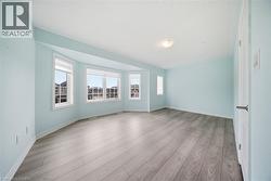This room features light blue walls, light-colored flooring, and a series of bay windows providing views of the surrounding neighborhood - 