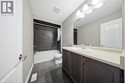 The bathroom features a vanity with a light-colored countertop and dark cabinetry, a large mirror, and a bathtub with dark tiled walls - 