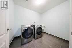 Dedicated laundry area featuring a tile floor, light blue walls, a white door with a brushed nickel doorknob, and modern front-loading washer and dryer units - 
