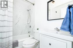 Bathroom featuring a white bathtub with a tile surround, a built-in toilet, and a vanity with a rectangular basin - 