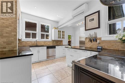 Kitchen featuring ceramic tile flooring, white cabinetry, dark countertops, and a brick-patterned backsplash - 110 Melrose Avenue S, Hamilton, ON 