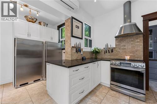 Kitchen featuring white cabinetry, dark stone countertops, stainless steel appliances, a tile backsplash, and light-toned tile flooring - 110 Melrose Avenue S, Hamilton, ON 