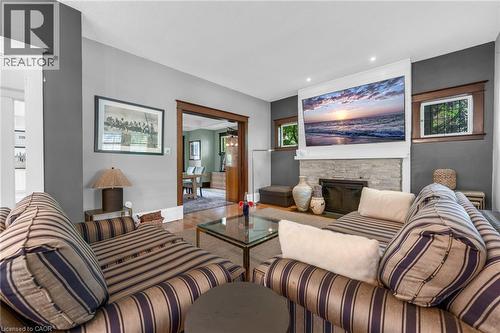 Living area featuring a stone-clad fireplace with a dark metal insert, flanked by two windows with wood trim - 110 Melrose Avenue S, Hamilton, ON 