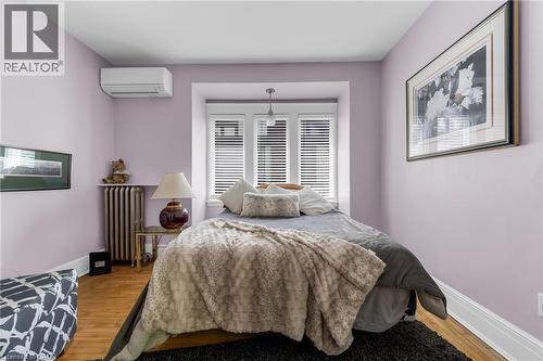 Recessed window bay with triple windows, wood-finish flooring, white baseboards, wall-mounted air conditioning unit, and a cast iron radiator - 110 Melrose Avenue S, Hamilton, ON 