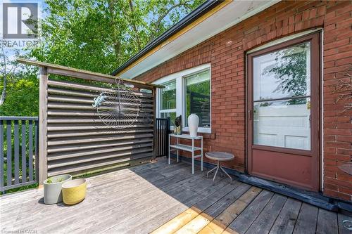 Brick exterior with a wood-finish deck, featuring a louvered wood screen, a single window, and a glass-paneled entry door - 110 Melrose Avenue S, Hamilton, ON 