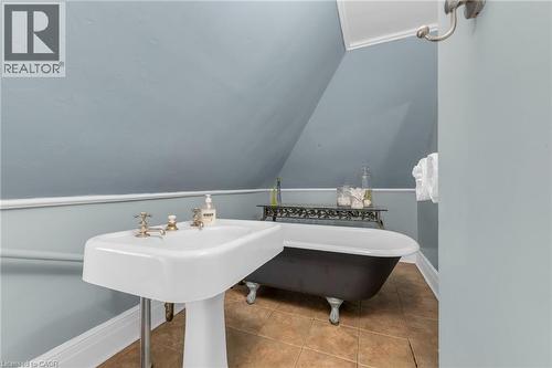 Pedestal sink with brass-finish fixtures, a stand-alone clawfoot tub, and warm-toned tile flooring - 110 Melrose Avenue S, Hamilton, ON 