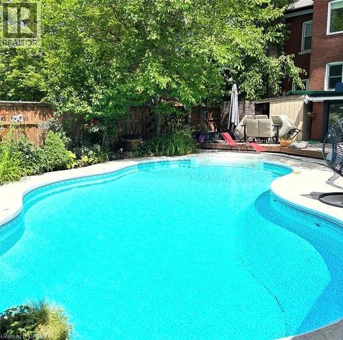 Inviting curved inground pool with integrated steps, surrounded by concrete coping and mature perimeter landscaping - 110 Melrose Avenue S, Hamilton, ON 