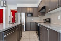 Kitchen featuring light tile patterned floors, under cabinet range hood, stainless steel appliances, a sink, and decorative backsplash - 