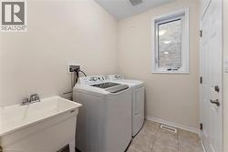 Clothes washing area with light tile patterned floors, washing machine and dryer, a sink, laundry area, and baseboards - 