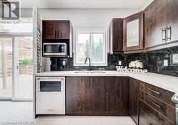 Kitchen featuring rich wood-finish cabinetry, light-colored speckled countertops, and a dark, patterned backsplash - 