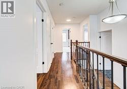 Upper-level hallway featuring wood-finish flooring, white paneled doors with matte black hardware, and a staircase with dark wood handrails and wrought iron balusters - 