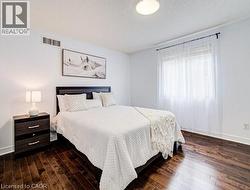Bedroom featuring rich wood-finish flooring, white walls, and a window with sheer curtains - 