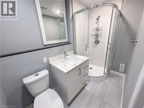 Contemporary bathroom featuring a corner glass-enclosed shower with white subway tile surround, a single vanity with a white countertop and integrated sink, chrome fixtures, and light-toned tile floor - 304 Lemon Grass Crescent Unit# B, Kitchener, ON 